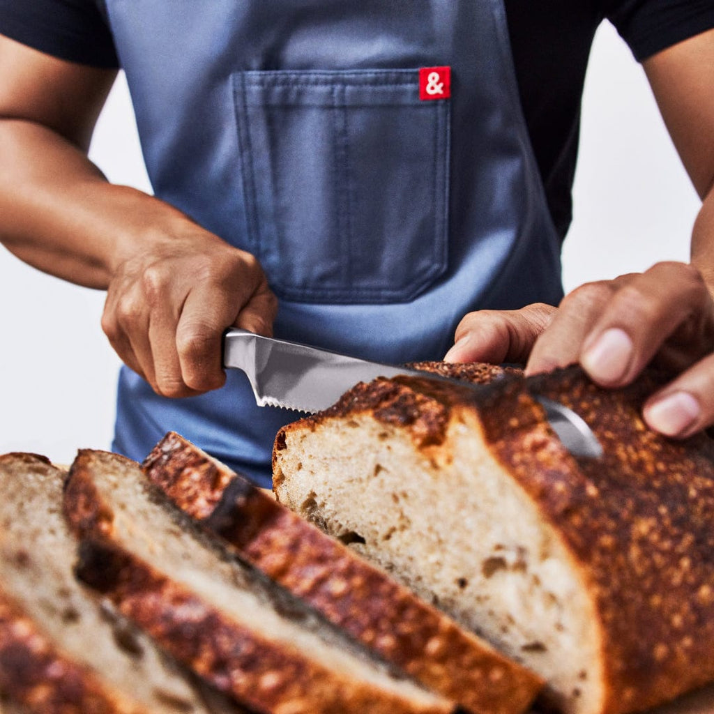 Cook in a denim apron slicing a crusty sourdough loaf with the bread knife