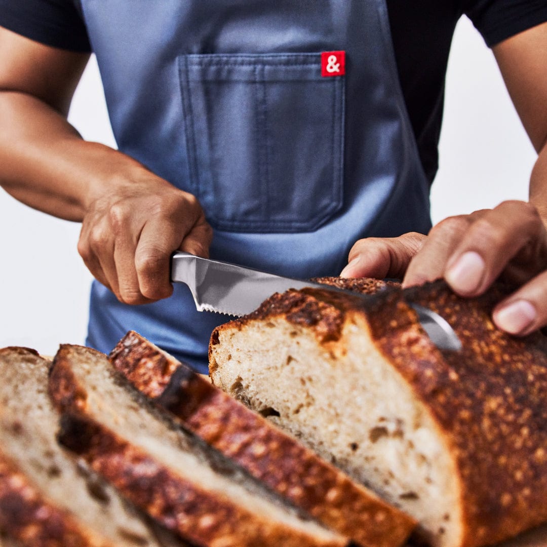 Cook in a denim apron slicing a crusty sourdough loaf with the bread knife