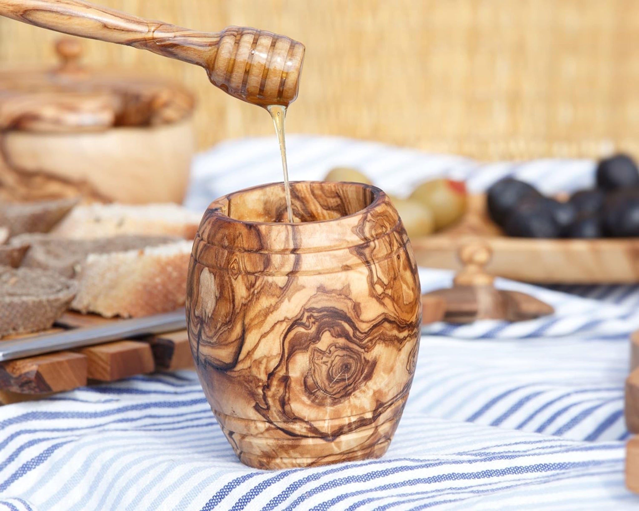 Olive wood honey pot with a dipper drizzling honey, beside bread and figs