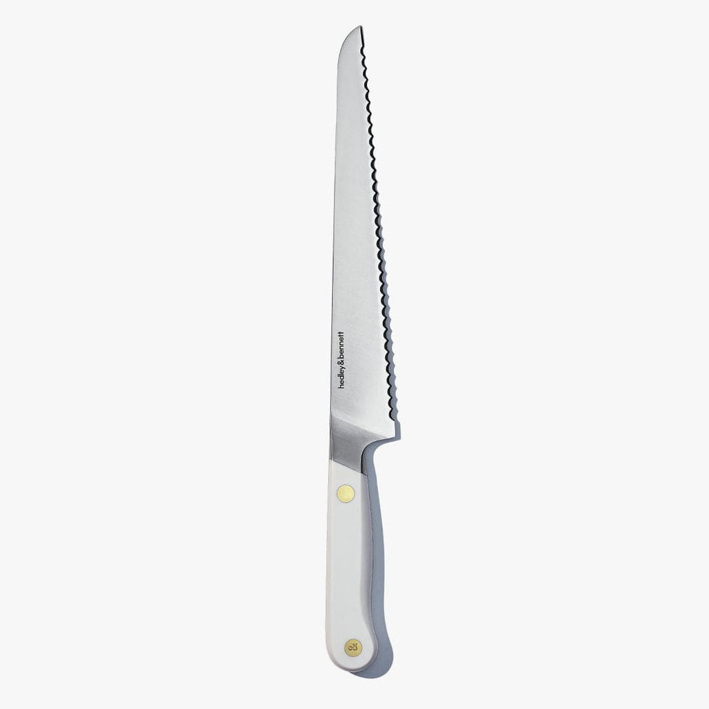 Serrated bread knife with a white handle and brass pin, standing upright