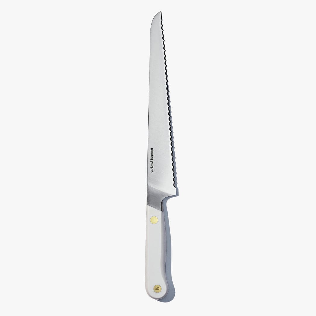 Serrated bread knife with a white handle and brass pin, standing upright