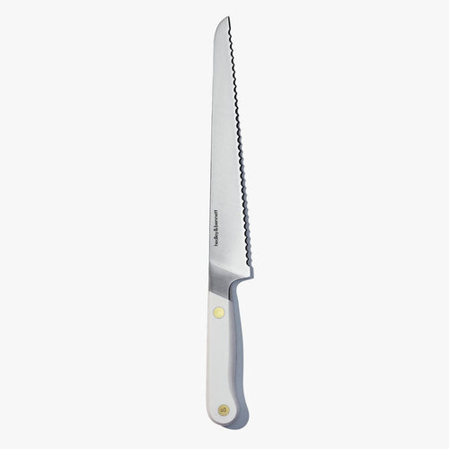 Serrated bread knife with a white handle and brass pin, standing upright