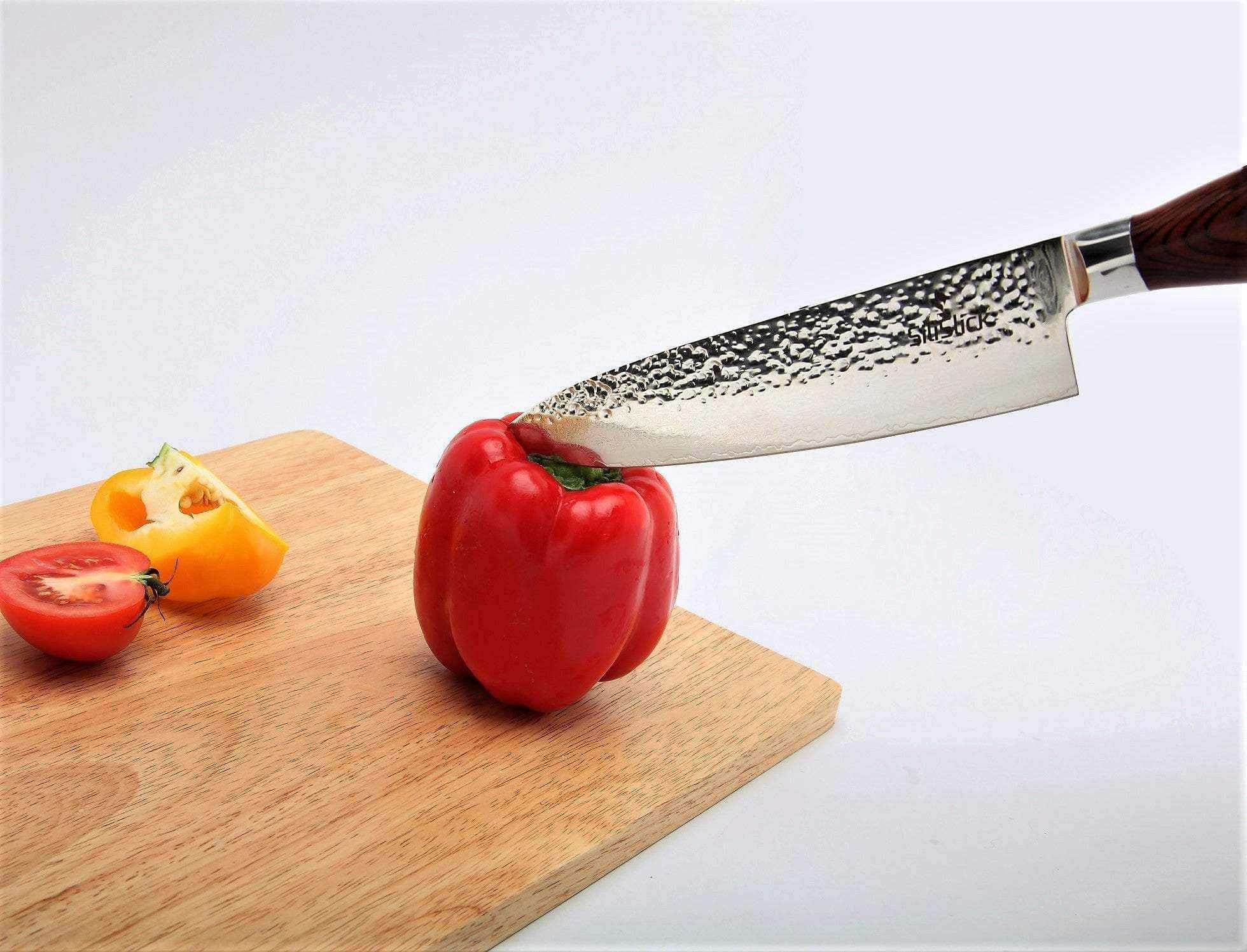 Hammered Damascus blade slicing a red bell pepper on a wooden cutting board