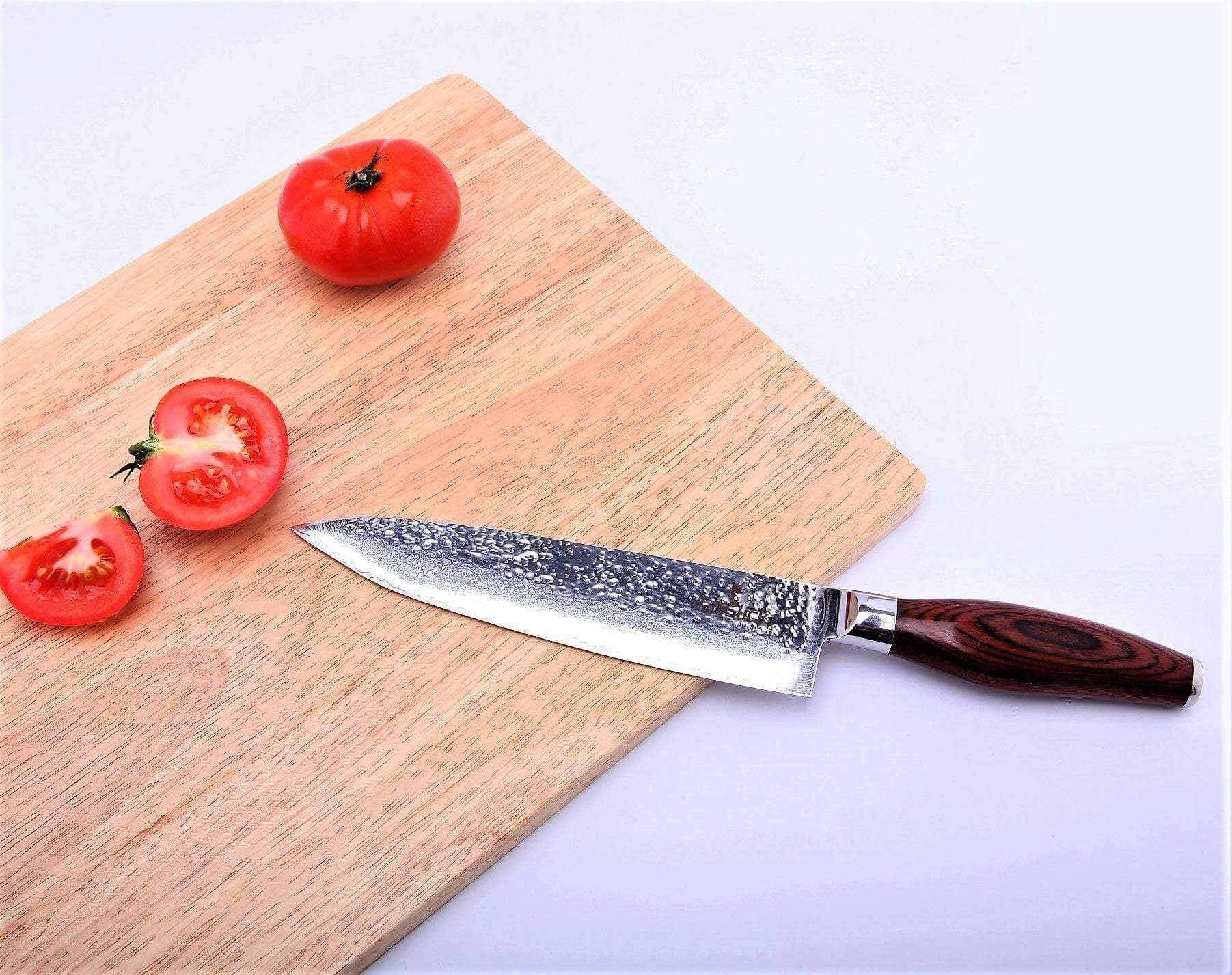 Damascus chef knife on a cutting board beside halved tomatoes