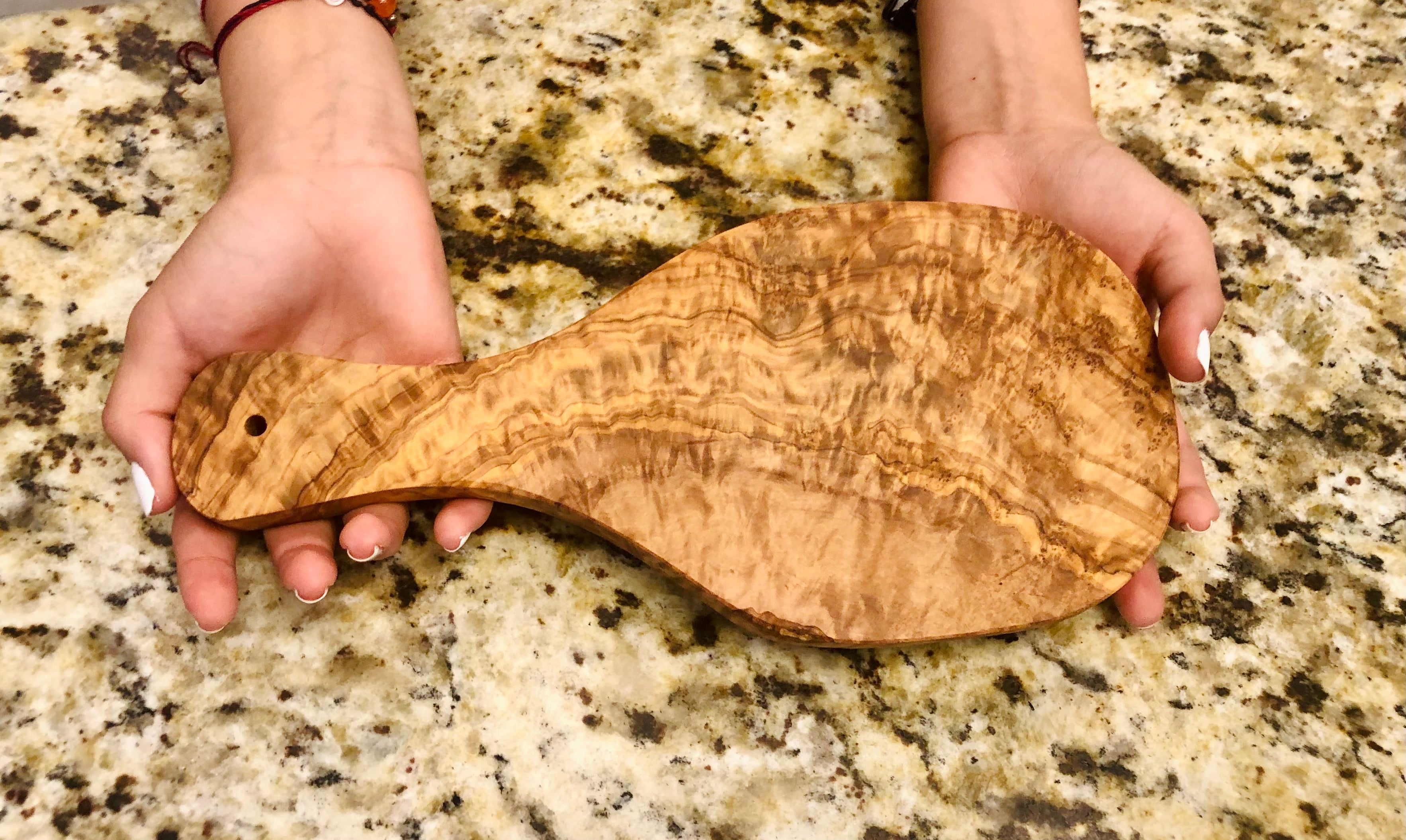 Two hands holding the olive wood cutting board above a granite counter, showing its size