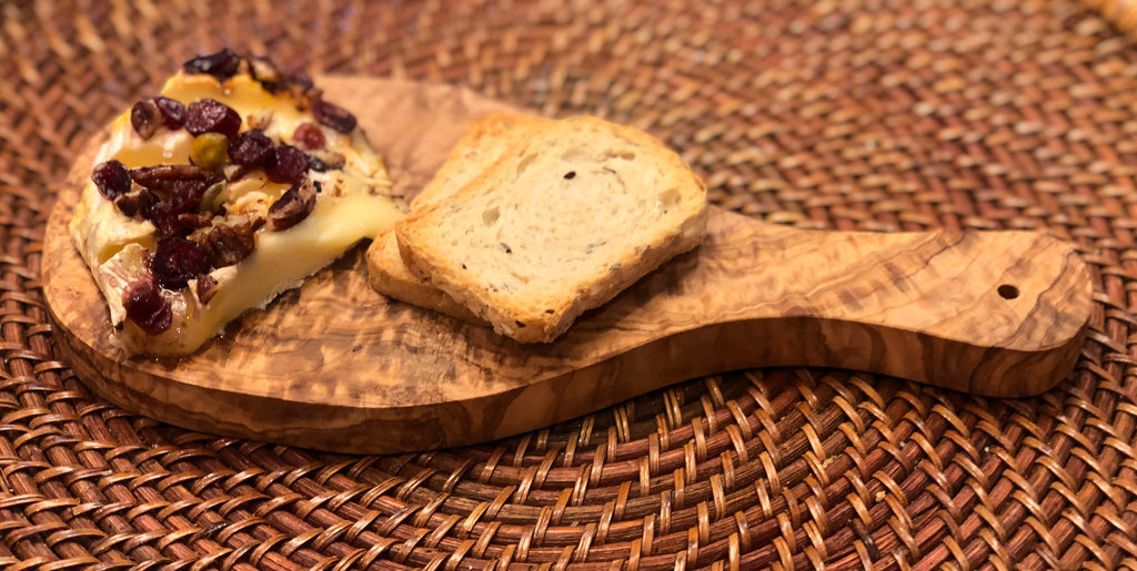 Baked brie with cranberries and a slice of toast served on the olive wood board on a woven placemat
