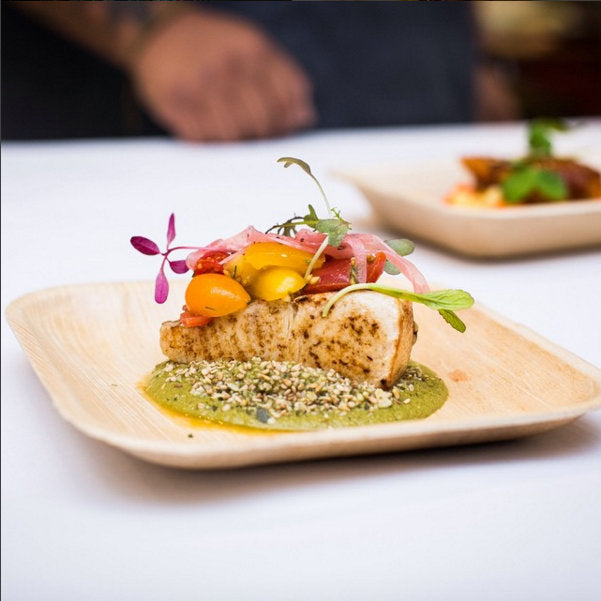 Chef plating a composed dish on a palm leaf plate