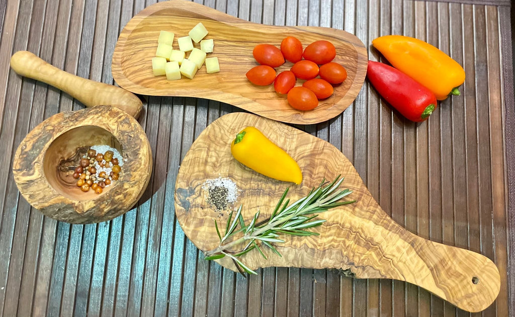 Olive wood board, bowl and mortar arranged with fresh vegetables and herbs