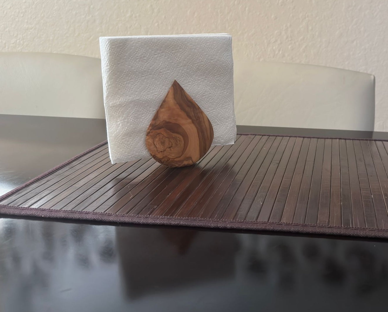 Olive wood napkin holder filled with white napkins on a dark bamboo placemat