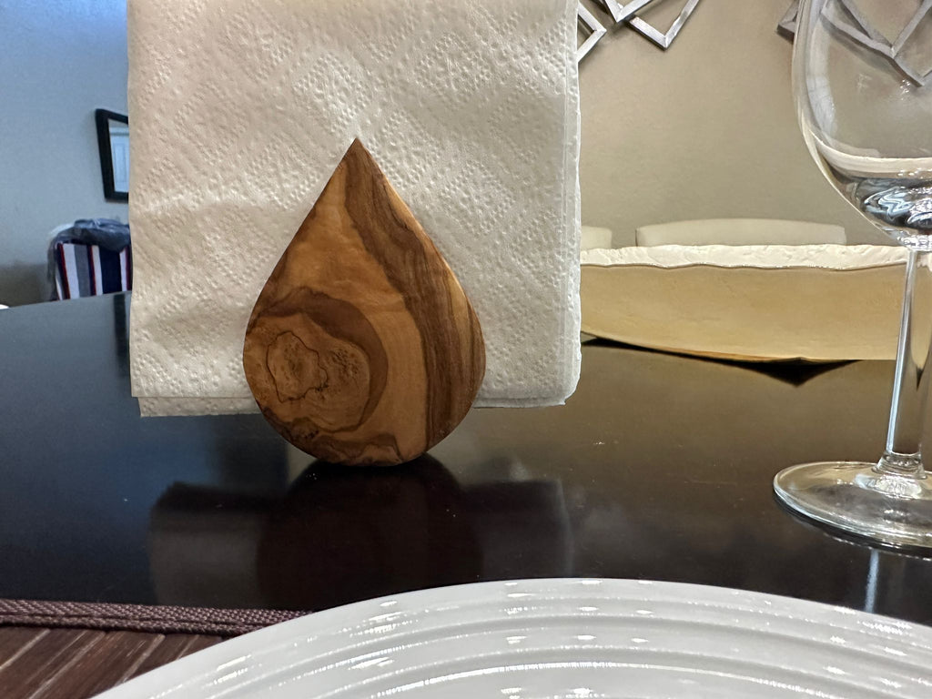 Olive wood napkin holder holding napkins at a set place with a wine glass and white plate