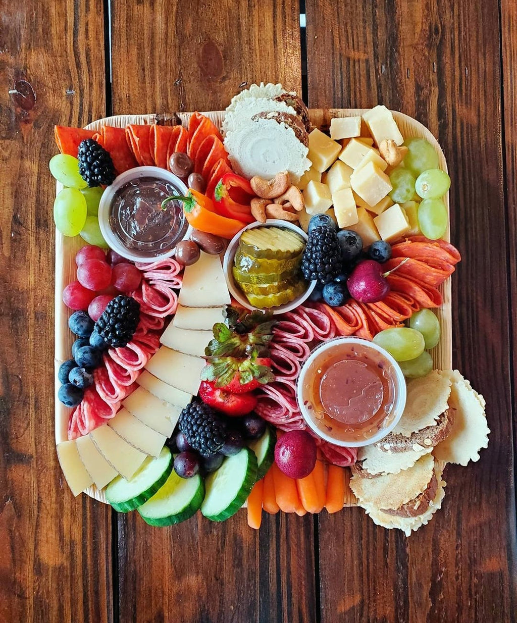 Palm leaf grazing board on a wooden table with charcuterie, cheese, fruit and dips
