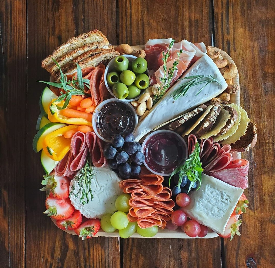 Palm leaf platter loaded with cured meats, olives, cheese and crackers on wood