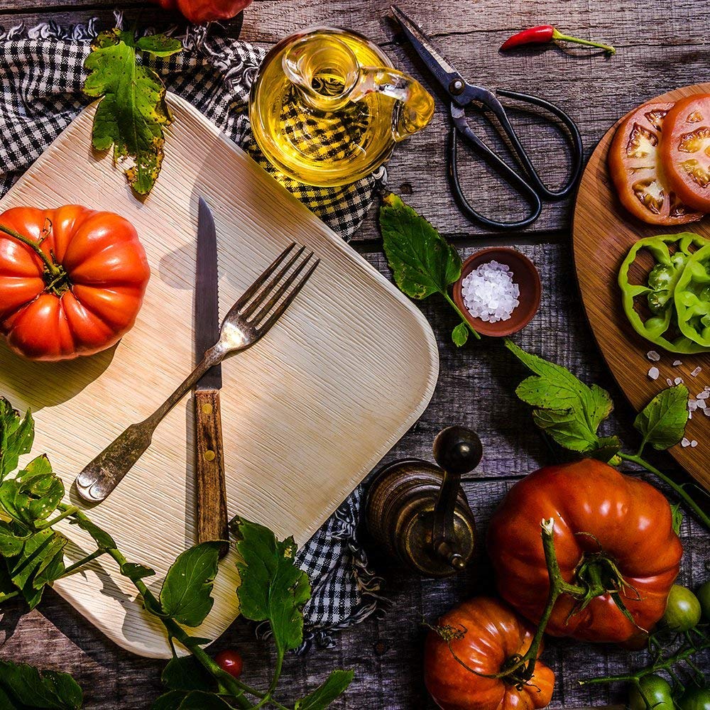Palm leaf plate set with cutlery among heirloom tomatoes and olive oil