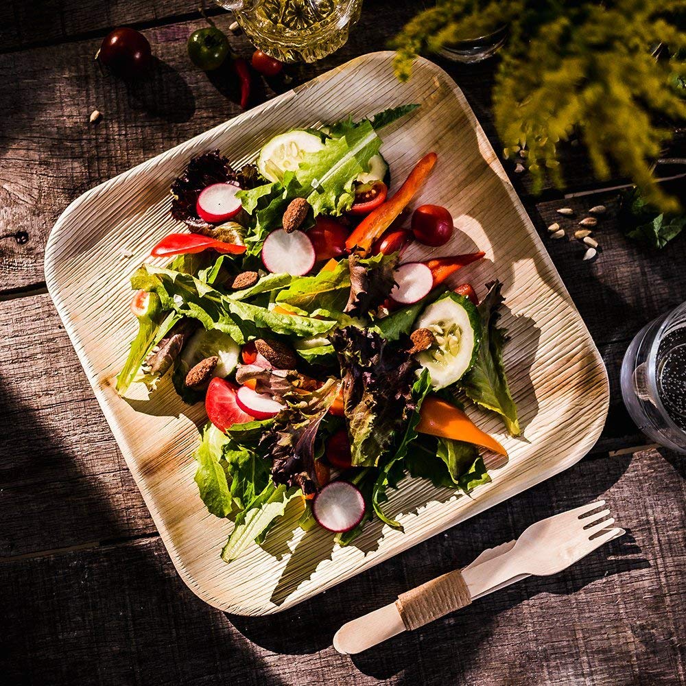 Fresh salad served on a palm leaf plate with a wooden fork on a dark table