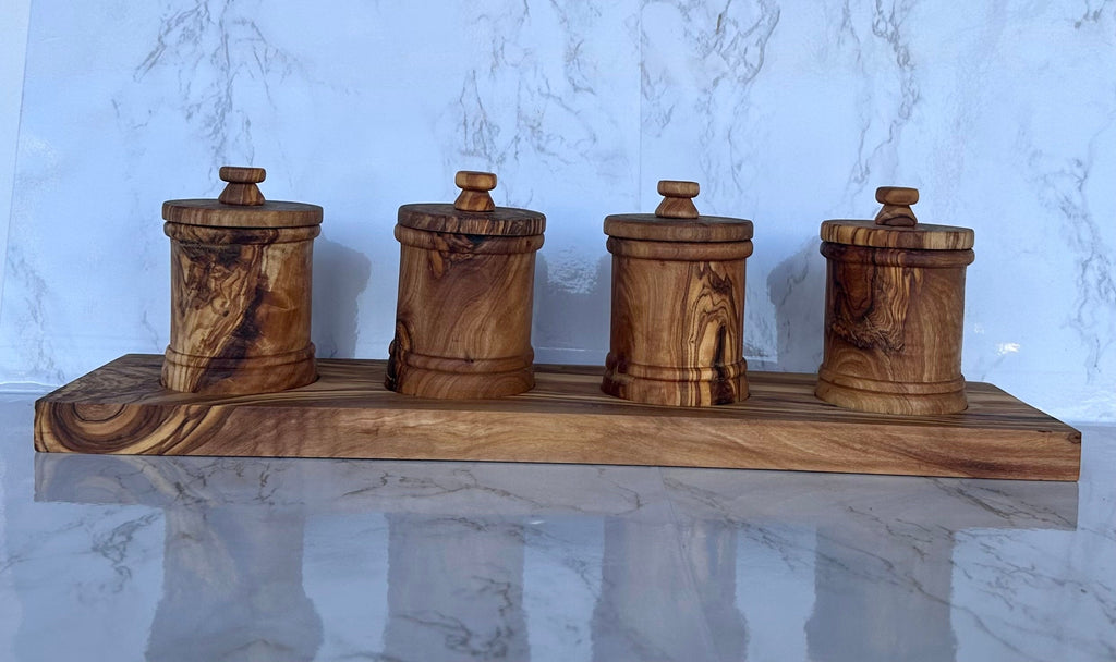 The four-canister olive wood set on its base, shown against a marble backdrop