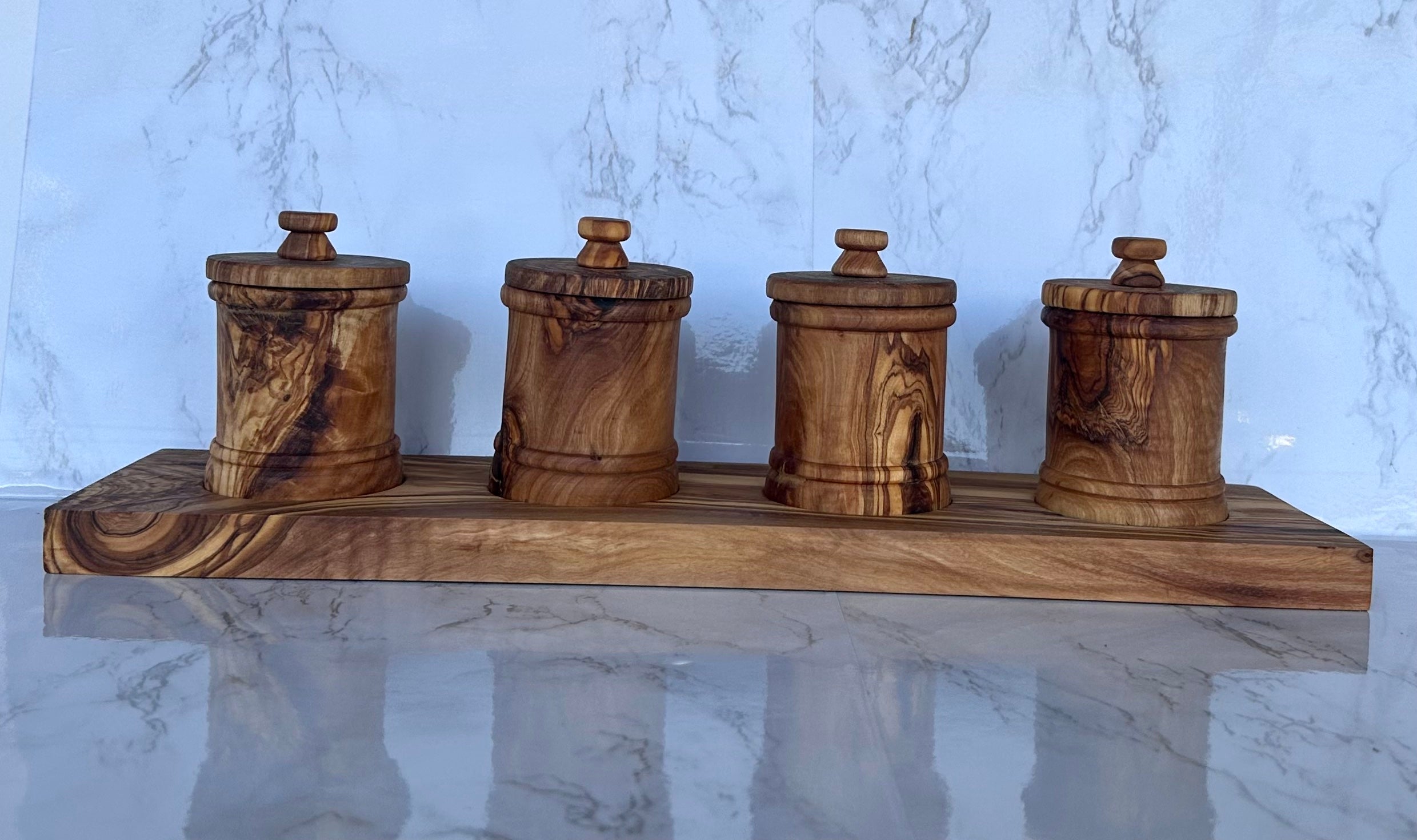 The four-canister olive wood set on its base, shown against a marble backdrop