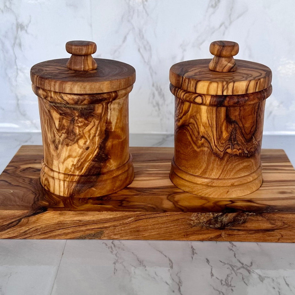 The two-canister olive wood set on its base, on a marble counter