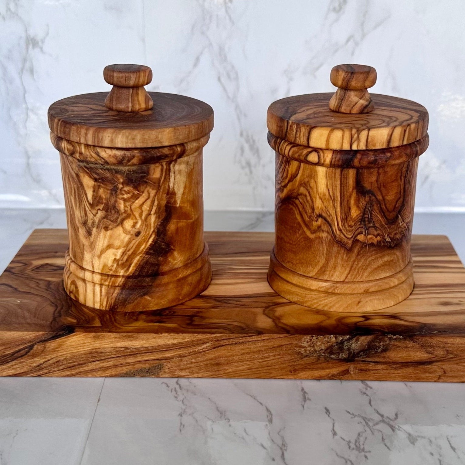 The two-canister olive wood set on its base, on a marble counter