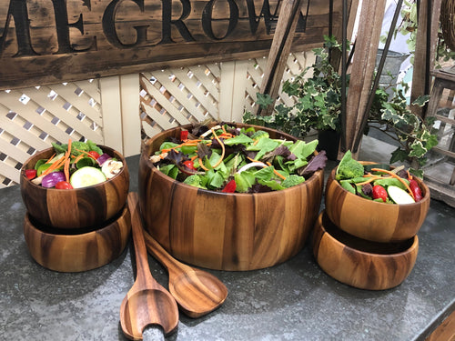 The acacia salad set filled with mixed greens, shown on a display table
