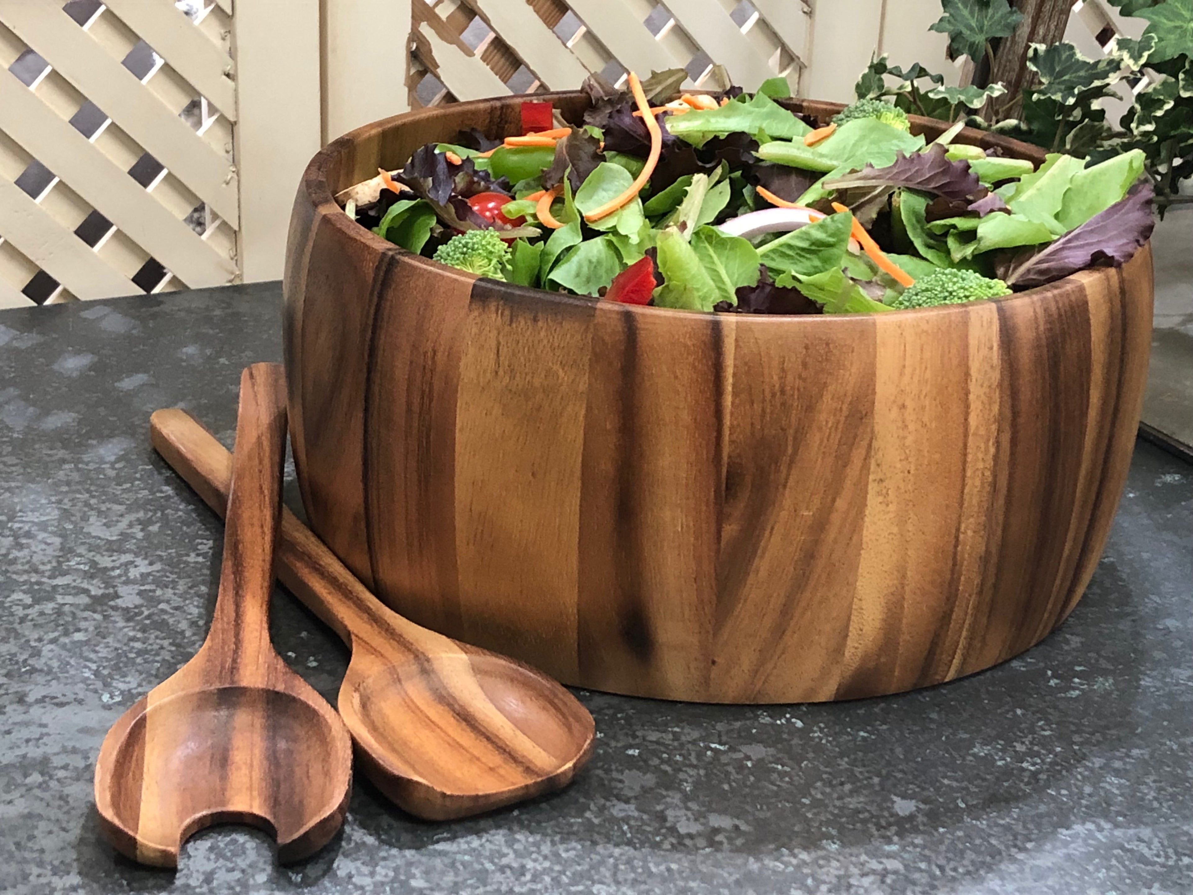 Acacia salad bowl filled with mixed greens, wooden servers resting alongside