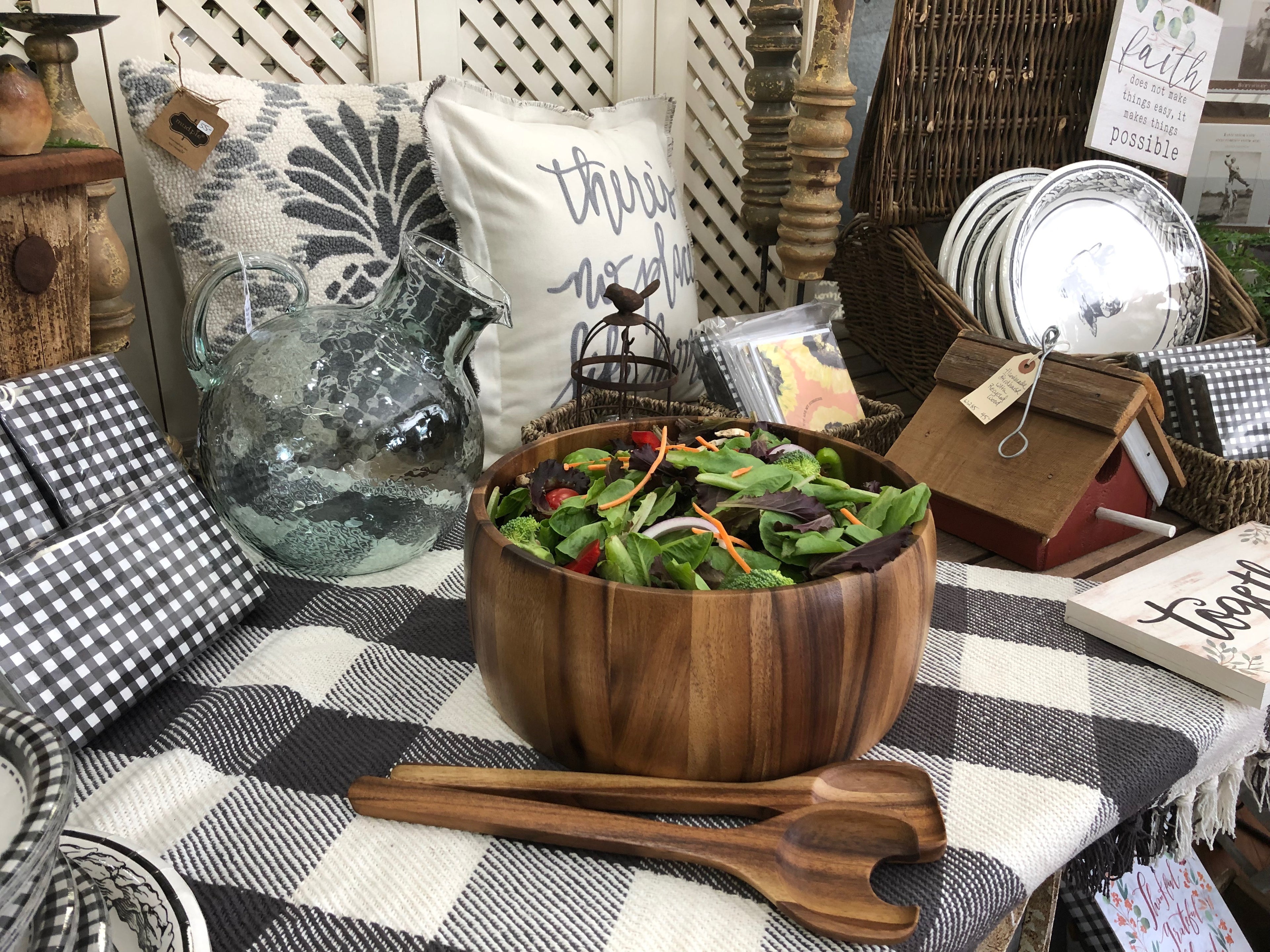 The acacia salad bowl filled with mixed greens on a checked cloth, servers in front