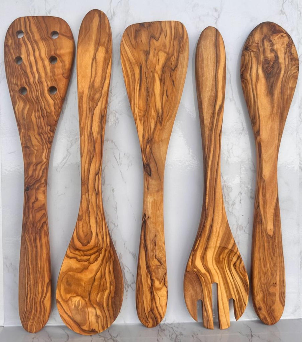 The five-piece olive wood utensil set laid flat on a marble surface